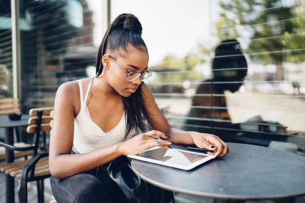 严肃的非洲裔美国女性 身穿时髦的眼镜 手持数码平板电脑打字短信在网上聊天 专心致志的非洲裔美国女性博主查看收入邮件和通知 — 图库照片
