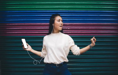 Genç Asyalı kadın, modern kulaklıklarla müzik listesinden keyif alıyor açık havada kaliteli ses dansı yapan, kulaklıklı neşeli hippi kız, fotokopi uzayı olan cep telefonundan müzik dinliyor.