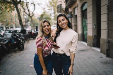 Şehir merkezinde yürürken kameraya gülen neşeli turistlerin yarım boy portresi, akıllı telefon taşıyan Asyalı hippi kız ve İspanyol en iyi arkadaşıyla poz veriyor.