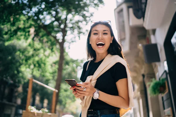 在这个阳光明媚的城市里 一个快乐的女人通过与4G连接的智能手机看到了这个好消息 她非常高兴地看着摄像机 笑着从社交网站上看到有趣的内容 — 图库照片