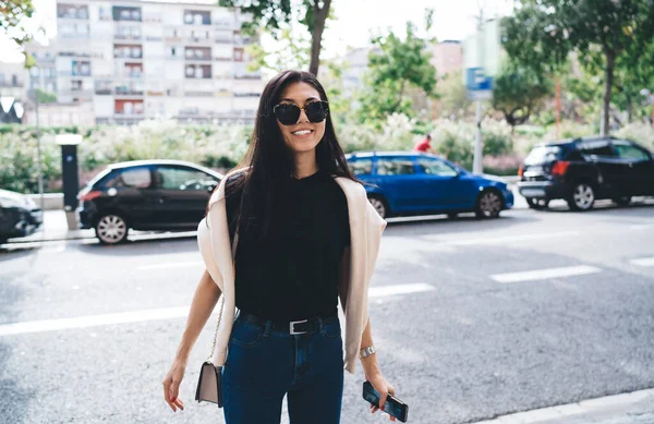 Half length portrait of cheerful asian female in sunglasses and trendy wear enjoying sunny day outdoors, smiling young pretty woman 20s dressed in trendy clothes visiting city during weekends