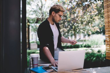 Gözlüklü ve resmi giysileri olan ciddi girişimcilerin düşük açısı. Tahta bankta otururken ve bahçede kahve molası sırasında bilgisayar kullanırken gazetelerdeki bilgileri kontrol ediyorlar.