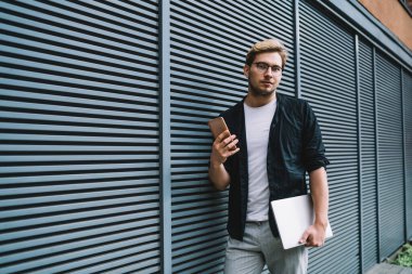 Genç odaklı siyah ceketli ve beyaz tişörtlü akıllı erkek yazın dizüstü bilgisayarını elinde tutuyor.