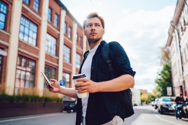 Sırt çantalı, günlük kıyafetlerle gezginlerin altında arkadaşlarıyla akıllı telefon mesajlaşması yaparak arka taraftaki kahve arama şehrini aydınlatıyor.