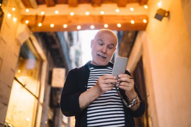 Düşük içerikli, günlük kıyafetli, cep telefonu ve gözlüklü, modern binadaki modern binanın önünde duran erkek.