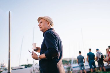 Düşük perspektiften, şapkalı, cep telefonlu ve kahveli yaşlı bir erkek.