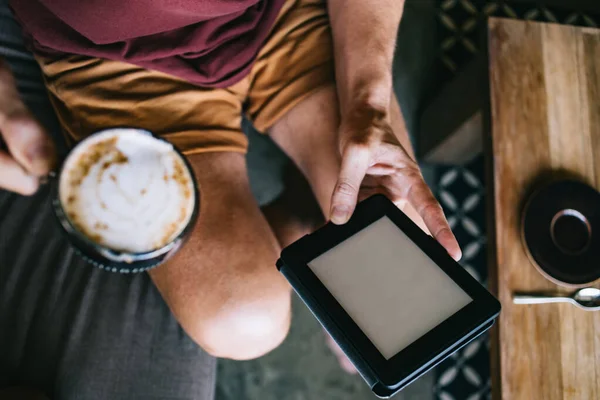 从上面看穿着休闲装的无名男子在现代咖啡店里浏览平板电脑和喝一杯热咖啡 — 图库照片