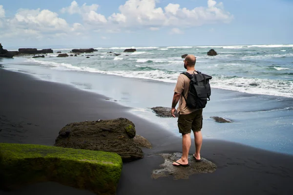 Yüksek açılı, kimliği belirsiz, sıradan kıyafetleri ve sırt çantasıyla gezen, fırtınalı deniz manzarasının keyfini çıkaran erkek yolcu.