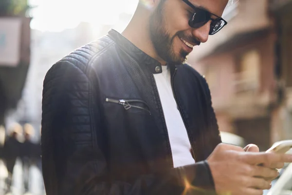 Crop Ethnic Male Trendy Jacket Sunglasses Smiling Browsing Mobile Phone — Stock Photo, Image