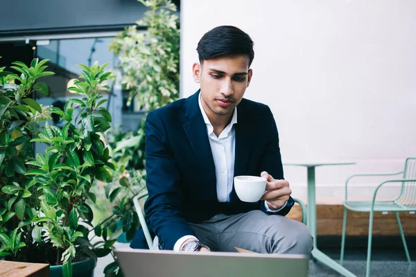 Pensive Etnische Mannelijke Werknemer Formele Pak Browsen Laptop Het Drinken — Stockfoto