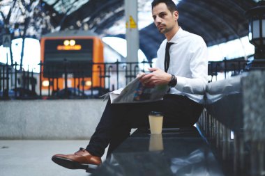 Resmi giysiler içinde düşünceli bir erkek çalışanın gazete okuyup trenden inmesini beklerken bakışlarını çevirmesi.