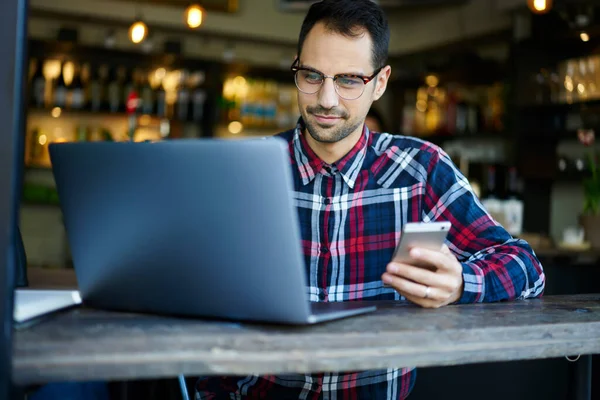 Yakışıklı Esmer Erkek Ekose Gömlekli Netbook Göz Gezdirirken Cep Telefonuyla — Stok fotoğraf