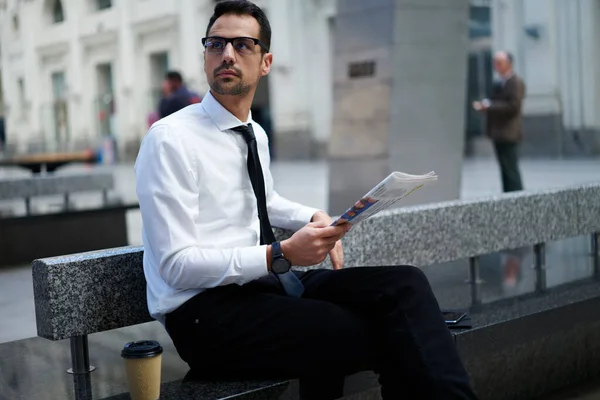 真剣な焦点を当てた男性マネージャー上品な服と眼鏡石のベンチに座って新聞を手にし コーヒーを飲みながら行く — ストック写真