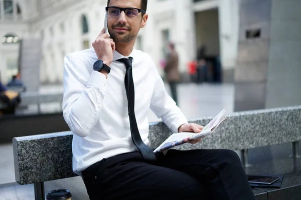 穿着正装 衣着得体的男性创业者 手拿着报纸坐在石凳上 在智能手机上聊天 — 图库照片
