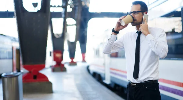 전화로 대화를 나누며 기차대에서 기차를 기다리고 커피를 마시는 사업가 — 스톡 사진
