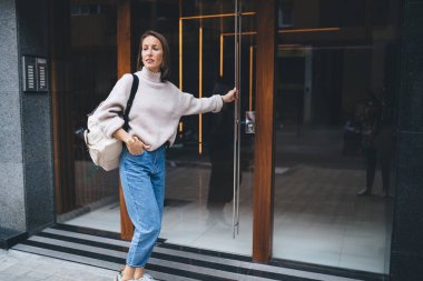 Sırt çantasıyla gezen ve taksiyi beklerken modern binanın cam kapısının yanında el ele tutuşarak bekleyen kadın turist.