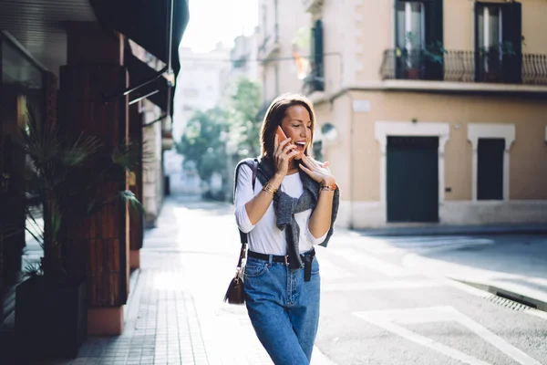 阳光明媚的日子里 身穿休闲装 身穿便服 面带微笑的高加索女人在城市街道上用手机交谈 积极的年轻女性在城市里用智能手机交谈 在街上漫游 — 图库照片