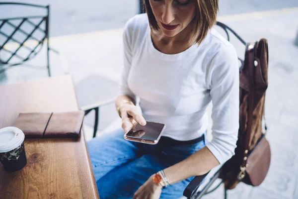 身着休闲装的成年女性坐在桌旁 手持智能手机和咖啡 在户外咖啡店浏览互联网 — 图库照片
