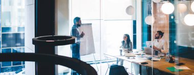 İş dünyasının lideri, yeni projeyi günlük kıyafetler giyen sakallı bir adamla masaya oturan siyah saçlı bir kadınla tartışıyor.