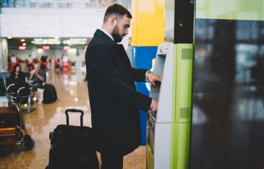 Havaalanına gittikten sonra ATM 'den para çekmek için resmi kıyafetler giyen Kafkasyalı işadamının yan görünüşü, şirket müdürü banka kartının pin kodu korumasını girdi
