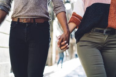 Güneşli bir günde şehir caddesinde birlikte yürürken günlük giysiler içinde el ele tutuşan isimsiz, çok ırklı, genç, romantik bir çift.