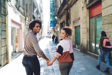 Şehrin eski bir bölgesinde dar bir yolda yürürken ve omuzlarının üzerinden bakarken sıcak kazaklı turistlerin arka plandaki mutlu genç çeşitliliği.