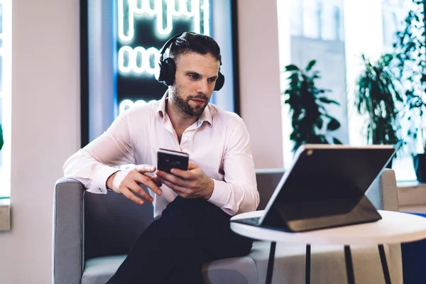 Caucasian businessman in earphones watching video webinar using bluetooth on touch pad and smartphone technology, successful professional in headphones connecting to 4g wireless internet on devices