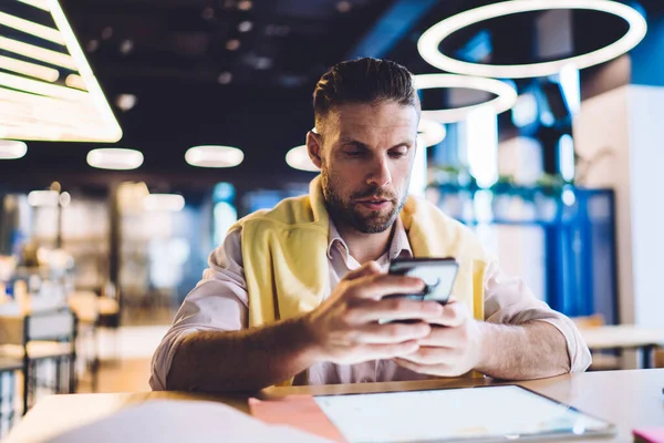 Caucasian male blogger in smart casual wear using cellular device for online mobility and network messaging, millennial man typing text while authorize on website for update web information