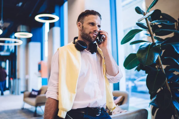 Handsome Caucasian businessman making cellphone consultancy conversation for discussing mobility connection, millennial coworker with bluetooth earphones using smartphone application for talking