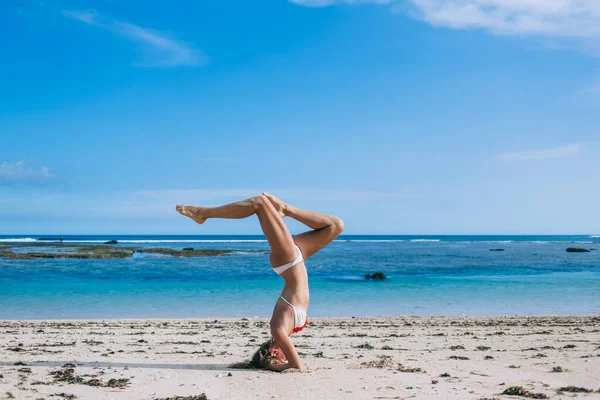 在阳光普照的海滨胜地练习希萨纳瑜伽平衡时 身穿泳衣的年轻苗条身材女子的侧观 — 图库照片
