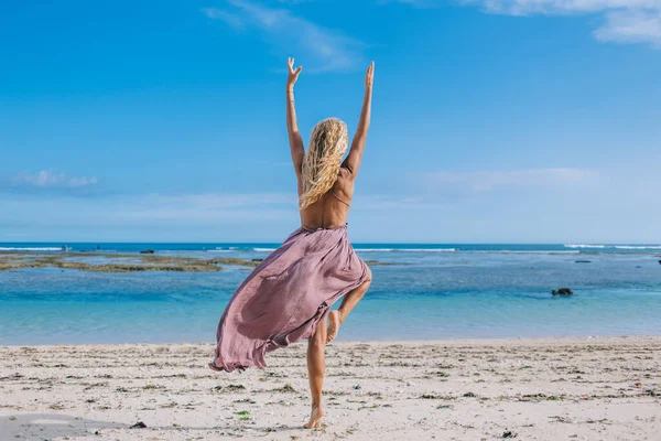 夏季在热带海滨练习瑜伽平衡时 看到穿着淡紫色衣服的金发年轻女子在做Vrksasana姿势的倒影 — 图库照片