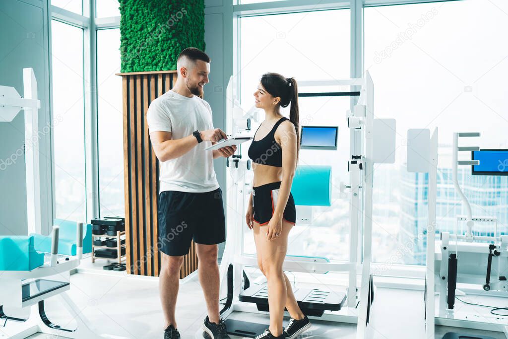 Slim young sportspeople in activewear standing in modern light gym and talking to each other while discussing sport exercises together