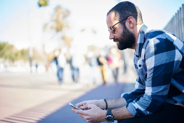 Oldalnézet Fiatal Hipster Férfi Alkalmi Ruhák Napszemüveg Böngészés Mobiltelefon Miközben — Stock Fotó