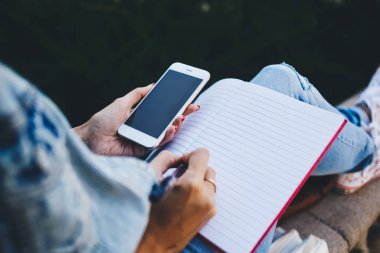 Yukarıdan gelen kot ceketli, kot pantolonlu, rahatlarken ve not defterine not alırken cep telefonunu karıştıran isimsiz bir kadın.