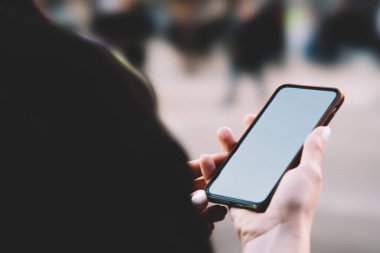 Siyah ceketli, yüzü olmayan, akıllı telefonlu bir kadının şehir caddesinde insan dolu bir şekilde dolaşması.
