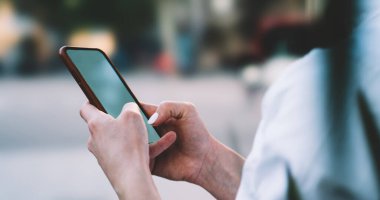 Yazın şehir parkında vakit geçirirken beyaz gömlekli, cep telefonuyla mesajlaşan kimliği belirsiz bir kadının yan görüntüsü