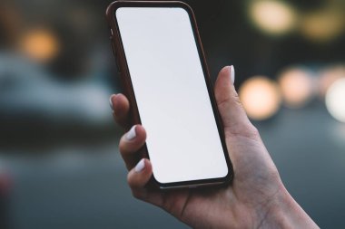 Beyaz manikürlü, yüzü olmayan, modern cep telefonlu, bulanık şehrin boş ekranlı beyaz eli.