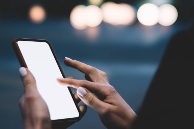 Kimliği belirsiz bir kadının sıradan kıyafetleriyle şehir sokaklarında vakit geçirirken cep telefonuna dokunuşunun yan görüntüsü.
