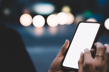 Akşam üzeri yol kenarında dikilirken cep telefonuyla boş ekran görüntüsü veren isimsiz bir kişi kırpın