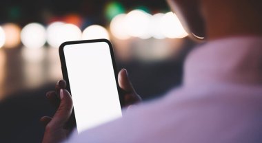 Çağdaş cep telefonundan mesajları kontrol eden isimsiz kişilere mesaj bırakın ve arka planda Bokeh ışıkları ile sokakta dururken internetten sohbet edin.