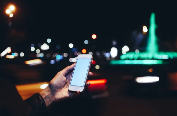 夜遅くに輝く都市の背景に立っている間白い空白の画面を持つ携帯電話を使用して匿名の女性をクロップ — ストック写真