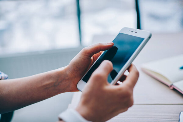 Сверху руки анонимного человека с современным мобильным телефоном и текстовым сообщением другу над деревянным столом с ноутбуком