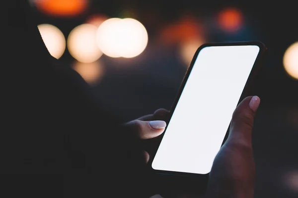 无法辨认的女性手持现代智能手机 屏幕上空白显示 而站在夜光背景下的夜街上 — 图库照片