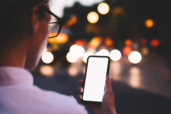 現代のスマートフォンの空白の画面上で眼鏡メッセージングで作物の匿名の若い女性のバックビューと夜の都市のボケの背景にインターネットを使用してオンラインチャット — ストック写真