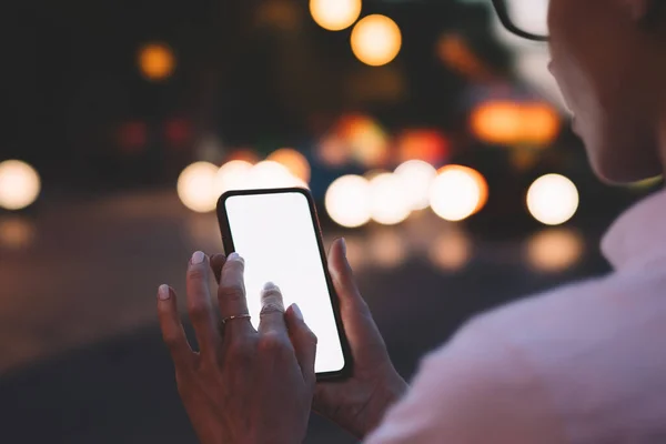 現代のスマートフォンの空白の画面上で眼鏡テキストメッセージで匿名の若い女性をトリミングし 夜の都市のボケの背景にインターネットを使用してオンラインでチャット — ストック写真