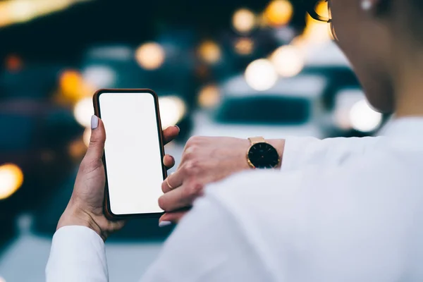 拥有修剪过的手的匿名女性在使用带有空白屏幕的现代智能手机时用时髦腕表检查时间的背景图 — 图库照片