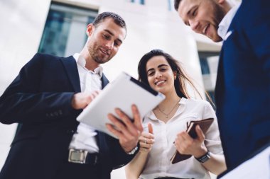 Düşük açılı mutlu iş arkadaşları sokak projesinde çalışırken gülümseyip tablet okurlar.