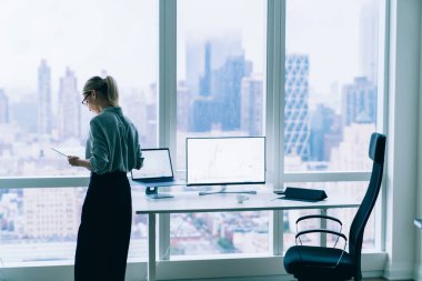 Tablet kullanarak pencerenin yanında duran ve bitcoin ticaretine para yatıran resmi kıyafet ve gözlüklü kadın tacirlerin arka plan görüntüsü