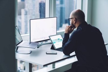 Resmi giysili ve gözlüklü isimsiz bir adamın yukarıdan görünüşü kripto para birimi bitcoin grafiğiyle çalışıyor.