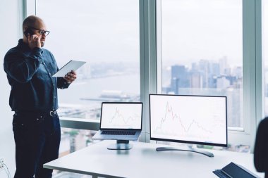 Resmi giysileri ve gözlükleriyle akıllı telefondan konuşan ve ofisteki not defterinden notlar okuyan konsantre iş adamlarının yan görüntüsü